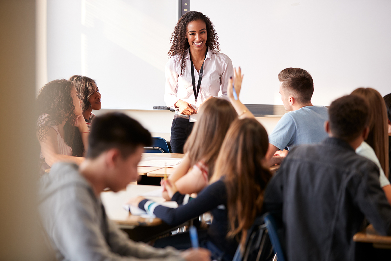 Female High School Teacher Standing In Front Of Interactive Whiteboard Teaching Lesson